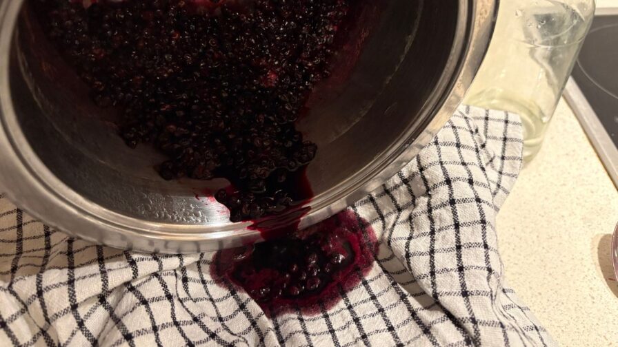 Gekochte Holunderbeeren werden durch ein Tuch gesiebt, um Holundersaft und Trester voneinander zu trennen