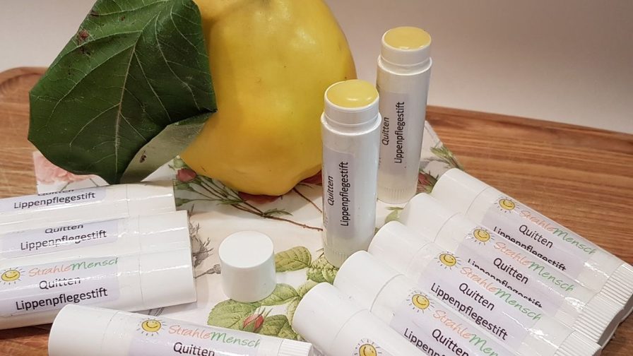 Selbst gemachte Lippenpflegestifte mit Quitte in weißen Hülsen, daneben eine gelbe Quitte und ein Quittenblatt