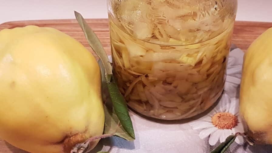 Glas mit Quittenschalen in Öl für den Kaltauszug, daneben zwei Quitten und Gänseblümchen